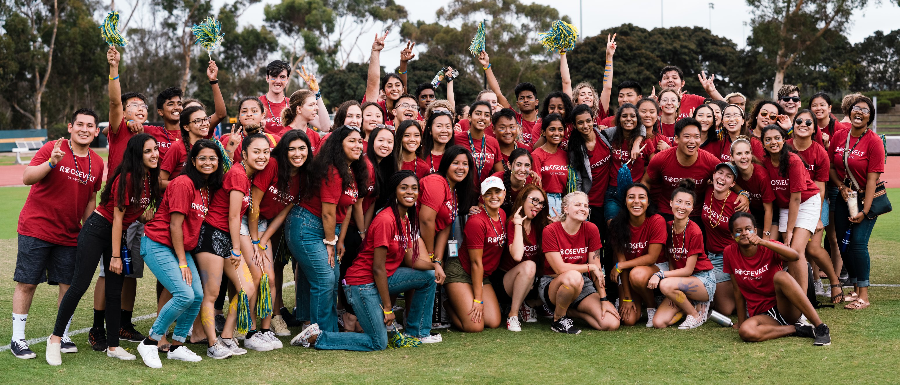 This image depicts approximately 50 students all wearing dark red "Roosevelt" shirts and smiling on a grass field after participating in UnOlympics.